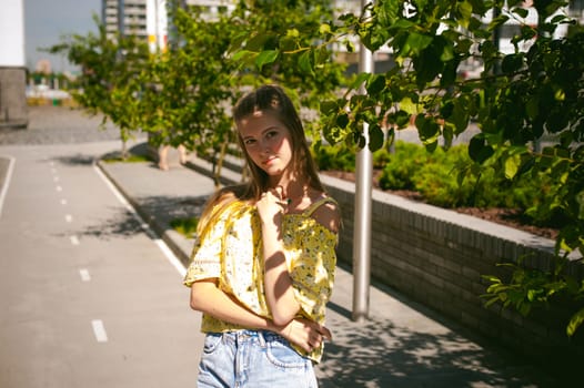 Young beautiful woman is strolling outdoors in the yard, against the backdrop of greenery and houses, warm summer sunny day