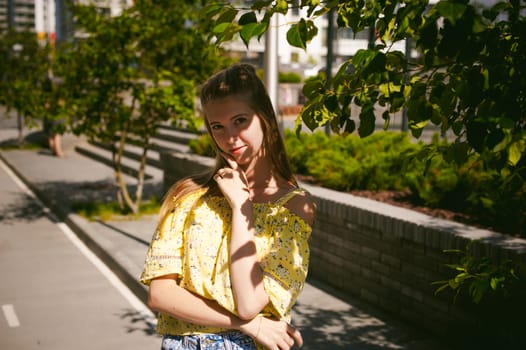 Young beautiful woman is strolling outdoors in the yard, against the backdrop of greenery and houses, warm summer sunny day