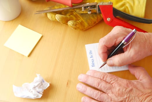Overhead of man writing a to do list with crumpled paper, notepad, coffee cup, gardening glove and grass cutters