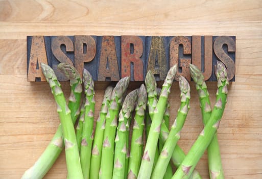 Fresh asparagus  on a cutting board with the word asparagus in old wood type