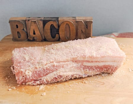 A piece of salted pork belly with the word bacon in wood type and room for text