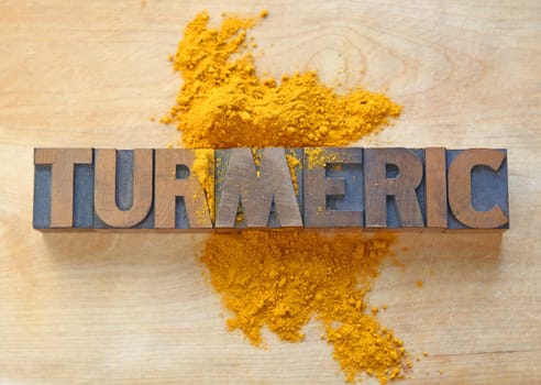 the word turmeric in antique old wood type on a cutting board with the spice sprinkled over