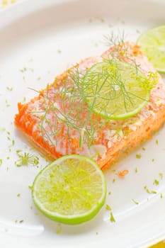 A serving of salmon roasted with garlic butter, garnished with fresh lime slices and dill