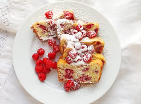 Slices of raspberry loaf cake dusted with powdered sugar on a white plate with fresh berries