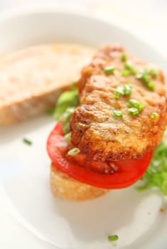 A battered and fried pork cutlet with tomato, chopped lettuce and scallions on artisan bread