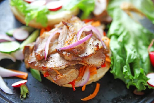 Garlic-roasted pork slices on a bun with raw onion, carrot, red bell pepper, radishes, lettuce and cucumber