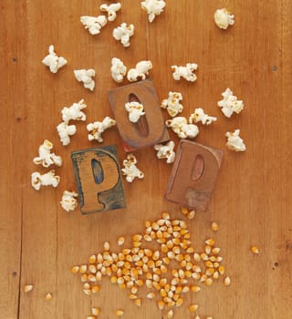 The word pop in wood letters with both unpopped and popped kernels of corn on a wood surface