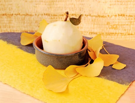 Peeled fruit in a small dish with autumn yellow ginkgo leaves on textured paper with copy space