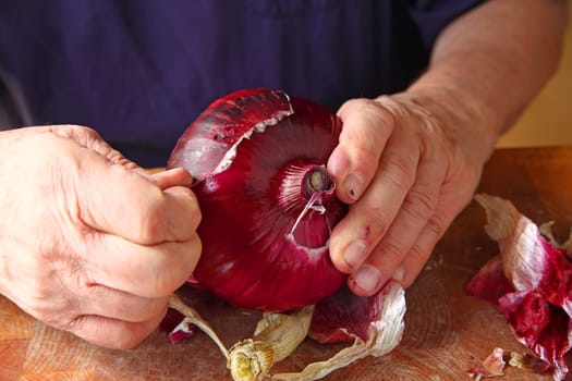 A man peeling the rough outer skin of a large red onion