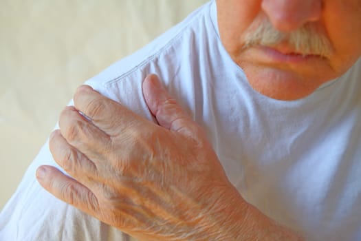 Senior man in a white t-shirt with his hand on a painful shoulder