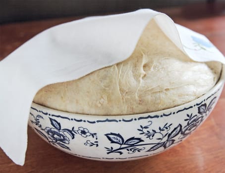 Bread dough rises in a bowl partially covered with a dish towel