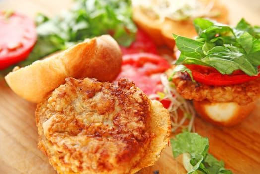 Battered and fried pork cutlets on crusty rolls with tomato and lettuce on cutting board