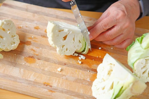 A man cuts up fresh cauliflower on a cutting board with copy space