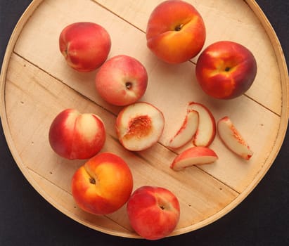 Fresh peaches, whole and cut up on a round wooden lid