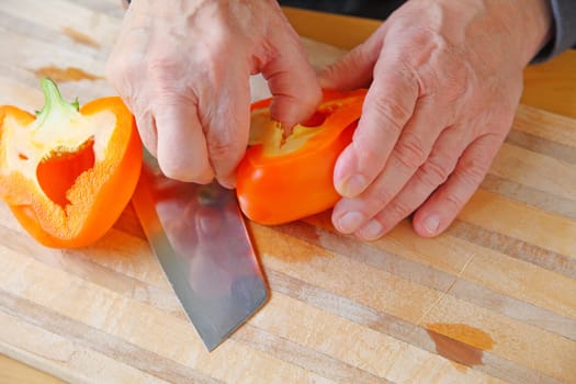 An older man removes seeds from a bell pepper on a cutting board with copy space