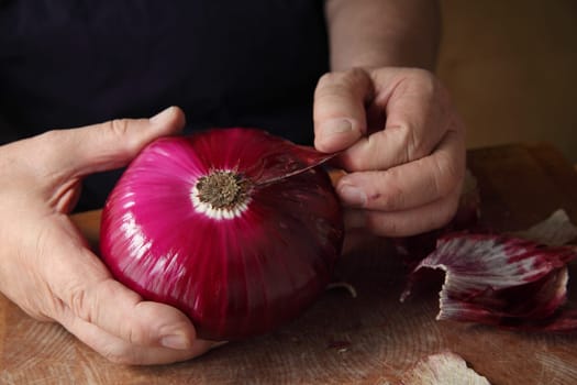 A man peels off an outer layer of a large red onion.