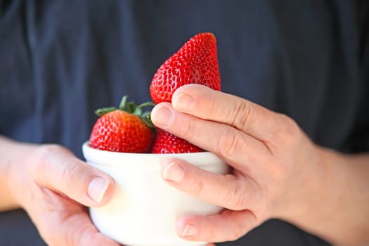 A man holds a white bowl of extra-large strawberries.