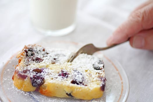 A man cutting into a slice of blueberry cake dusted with powdered sugar