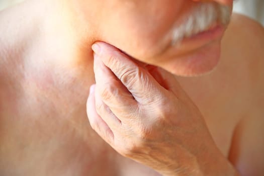 An older man touches his painful throat with his fingers