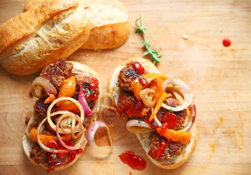 Meatballs with fried onions, orange bell peppers, ketchup and snipped fresh oregano on hard rolls with copy space