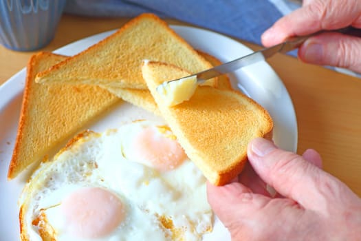 Fried eggs and toast on a platter with man buttering toast triangle