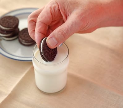 A man dips a cookie in a glass of milk with copy space