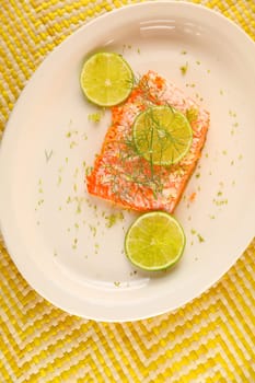 Overhead of salmon portion with garlic butter, fresh dill and lime slices