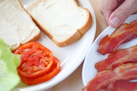 A man gets ready to put together a bacon, lettuce and tomato sandwich on white bread.