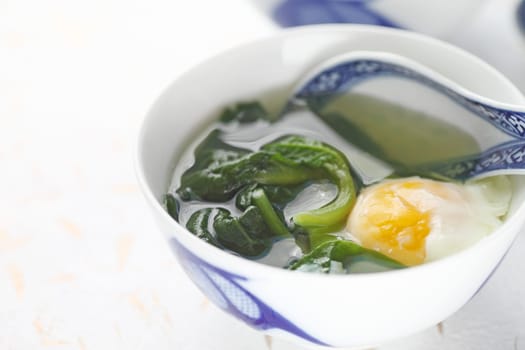 Malabar spinach soup with poached egg in Chinese bowl with spoon and copy space