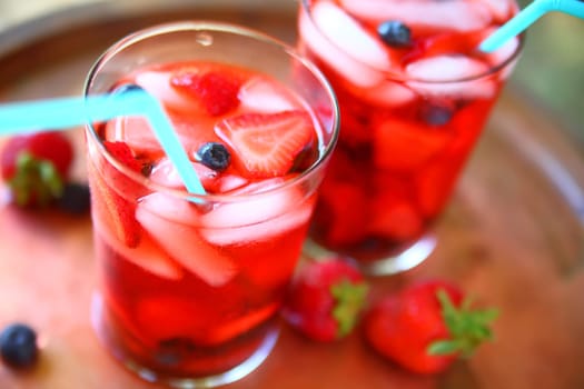 Two glasses of icy water with strawberries and blueberries