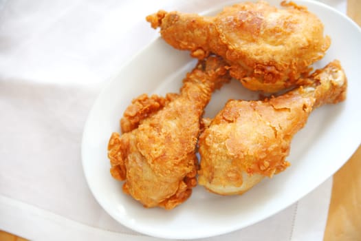 Three fried chicken legs on a white dish with a white napkin and copy space