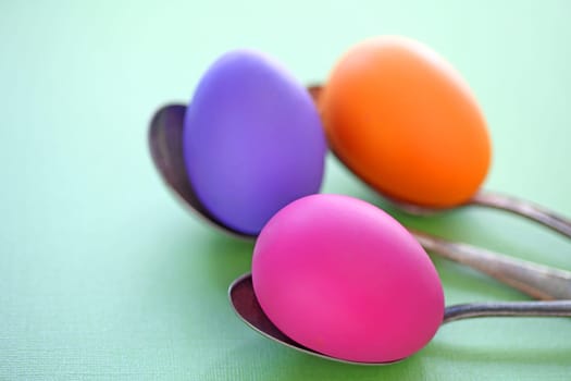 three Easter eggs on old spoons on a pale green background with copy space