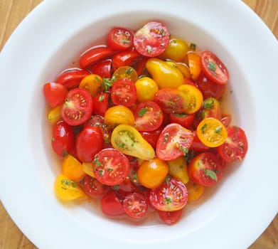 Assorted varieties and shapes of ripe cherry tomatoes marinating in a white dish from overhead