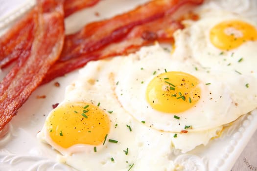 Platter with bacon strips and fried eggs topped with black pepper and fresh chives
