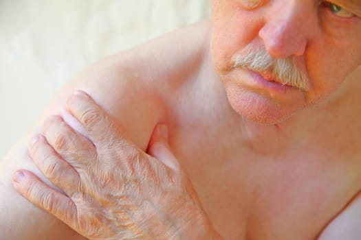 An older man with a hand on an aching shoulder joint
