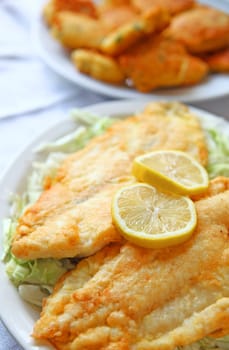 Battered and deep-fried catfish fillets on shredded cabbage with hushpuppies in the background