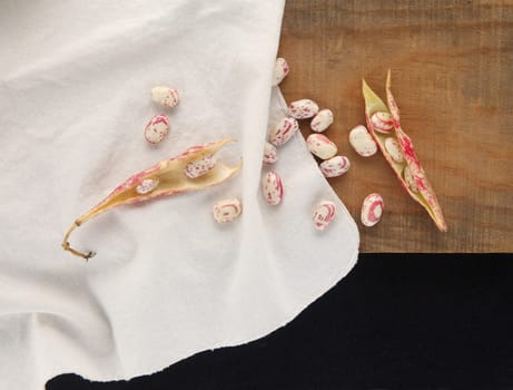 Overhead of cranberry beans, some in the shell, others loose on a white cloth on a wood surface with room for text