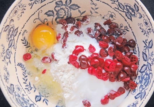 Chopped fresh cranberries with egg and flour in a blue and white mixing bowl
