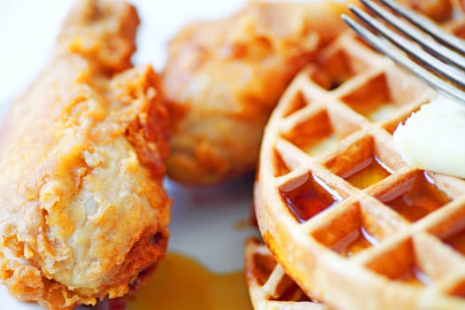 Closeup of fried chicken legs, Belgian waffles, butter and maple syrup with a fork