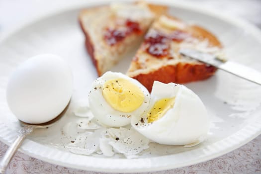 two boiled eggs, one half-shelled and broken apart, with toast spread with jam and butter, cut into triangles