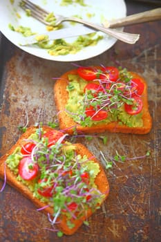 Avocado toast with cherry tomatoes and sprouts on old baking pan