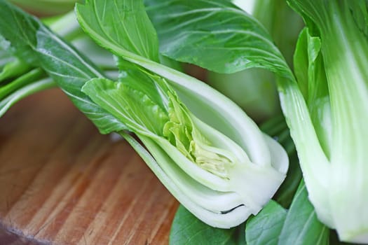 Fresh baby bok choy, one cut in half on cutting board with copy space
