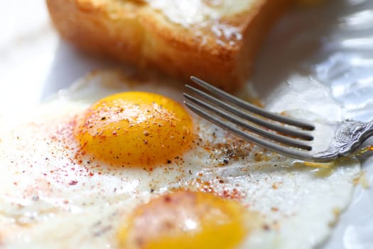 fried eggs  with smoked paprika and black pepper with fork and buttered toast