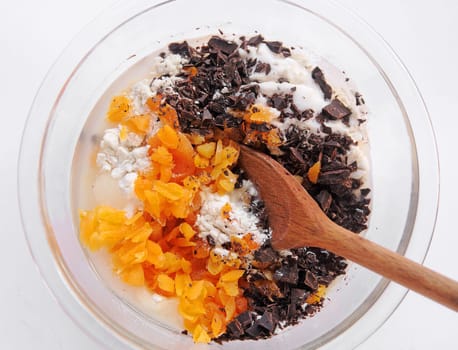 Overhead view of dark chocolate pieces, chopped dried apricots and flour in a glass mixing bowl