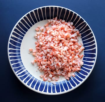 Cooked shrimp chopped in a dark blue and white bowl on a blue background