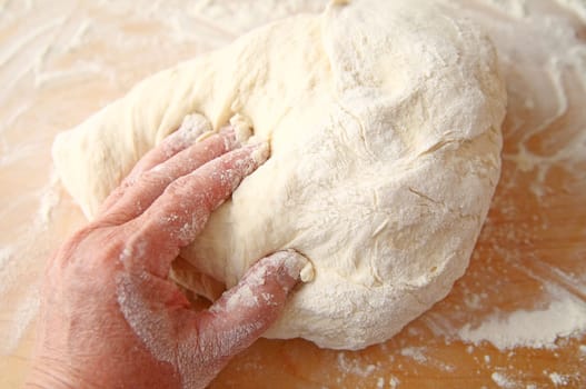Hand with dough and flour-covered fingers midway through dough kneading