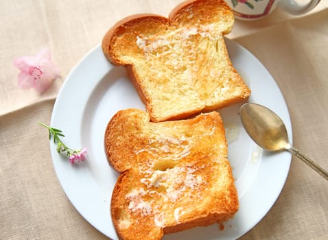 two slices of buttered brioche bread with unfiltered honey on white plate with spoon and teacup
