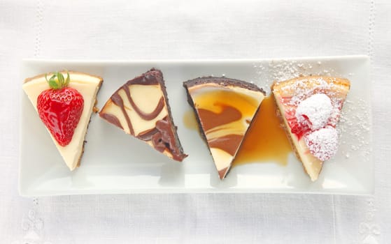 Four cheesecake portions topped with fresh berries, chocolate and caramel sauce