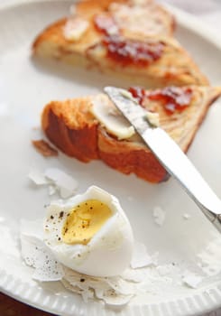 partially-peeled boiled egg with toast spread with butter and jam