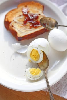 Partially peeled boiled and cracked eggs with cinnamon bread toast spread with strawberry jam